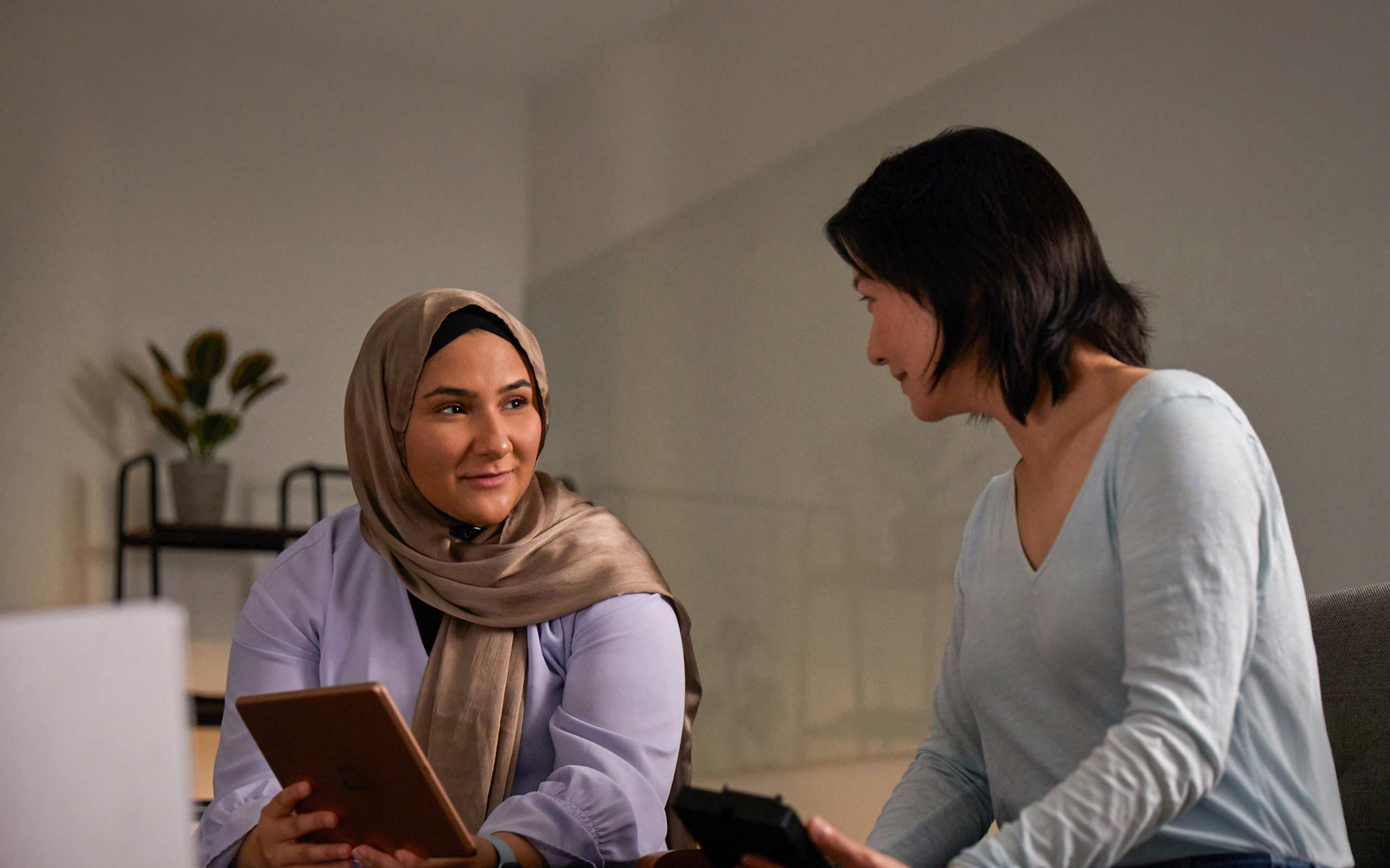 Two Apple Machine Learning and AI team members collaborating together, one holding an iPad and one holding an iPhone.