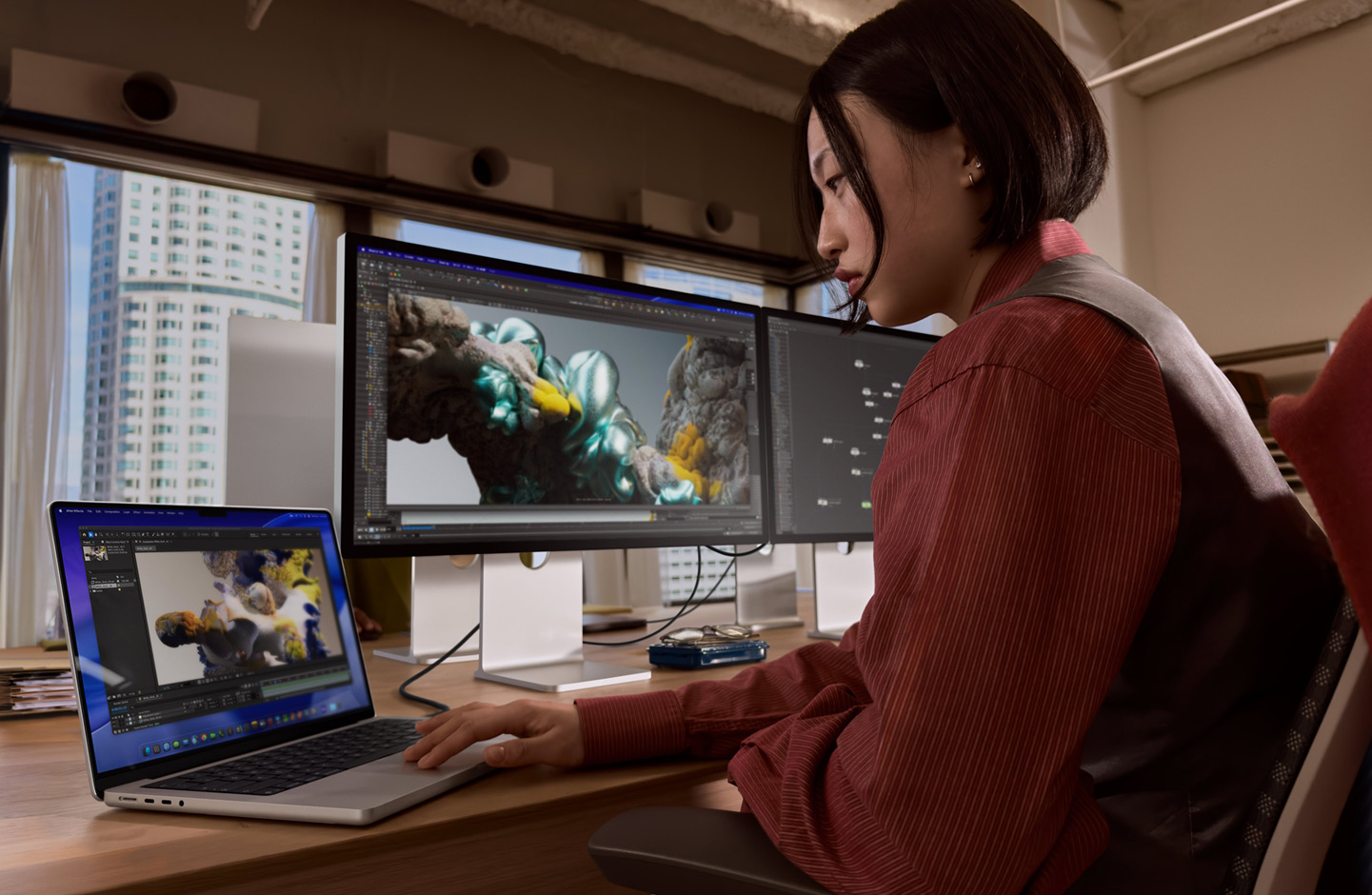 En person i et kontormiljø jobber på en MacBook-laptop som er koblet til Studio Display XDR via en Thunderbolt 5-port.