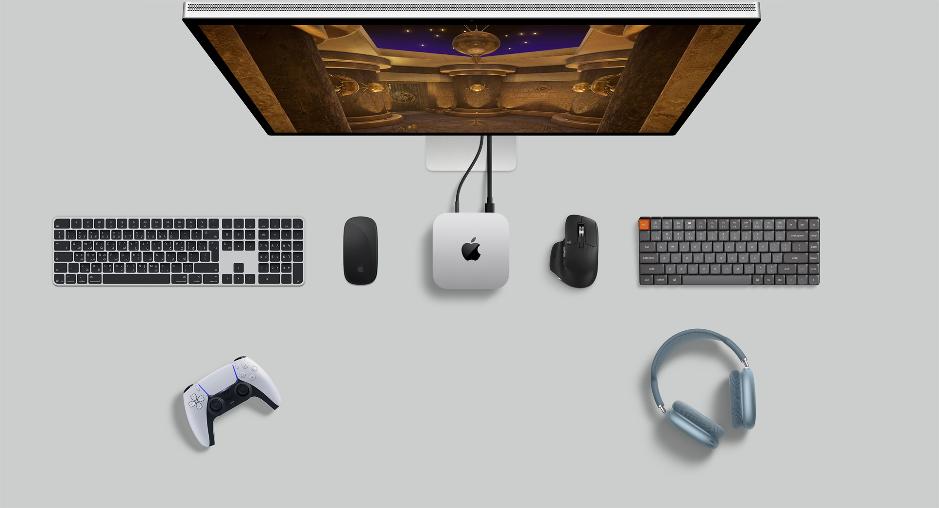 لقطة علوية لجهاز Mac mini ضمن إعداد مكتبي مع شاشة Studio Display، اثنتان من لوحات المفاتيح اللاسلكية، اثنان من أجهزة ماوس اللاسلكية، وحدة تحكم في الألعاب، وسماعات AirPods Max‏