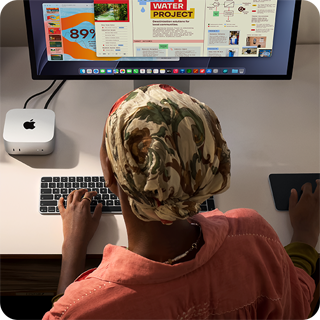 O persoană tastând la un birou cu un Mac mini, Studio Display conectat, Magic Keyboard, Magic Trackpad, diverse obiecte