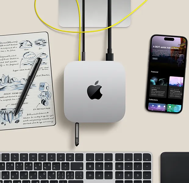 Mac mini 的俯視圖，展示銀色鋁金屬機身、圓角設計，以及機身中央的黑色亮面 Apple 標誌，透過連接線連接，隨身碟插在正面 USB-C 埠，Studio Display 支架部分可見，旁邊放著 iPhone、巧控板、含 Touch ID 的巧控鍵盤，以及手寫筆和電子墨水塗鴉板
