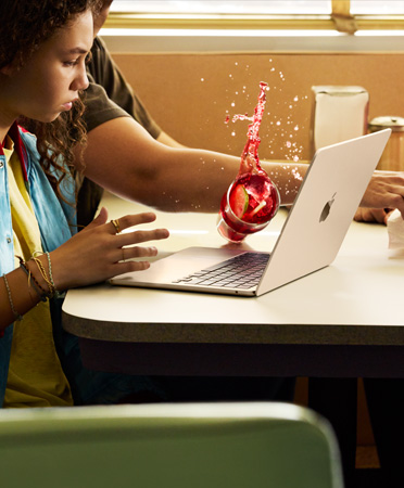 Seseorang sedang mengambil sesuatu di restoran, menumpahkan minuman dingin ke MacBook yang terbuka