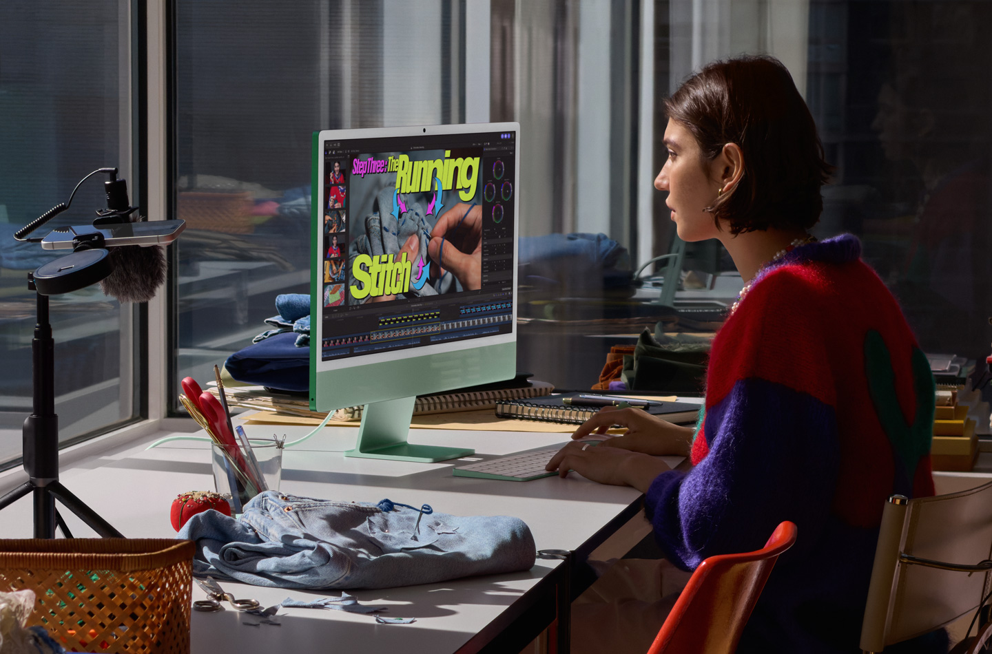 En person sidder ved et skrivebord med en grøn iMac, skriver på et Magic Keyboard og bruger en Magic Mouse, mens vedkommende ser en vejledning i syning