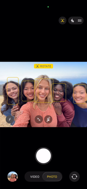 Vista frontal do ecrã do iPhone 17 Pro, a mostrar a funcionalidade Enquadramento central para fotografias e como tirar uma selfie de um grupo de pessoas, com os rostos em destaque