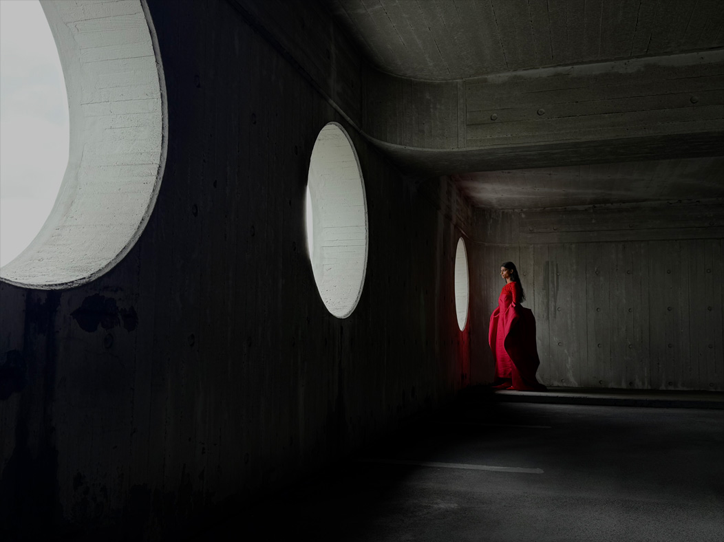 ผู้หญิงใส่ชุดเดรสยาวสีแดงยืนโพสท่าถ่ายภาพอยู่ในห้องว่างๆ แอปรูปภาพสลับเป็นทางยาวโฟกัสช่วงต่างๆ ตั้งแต่ 200 มม. ถึง 13 มม. เพื่อแสดงความสามารถของระบบกล้องระดับโปร