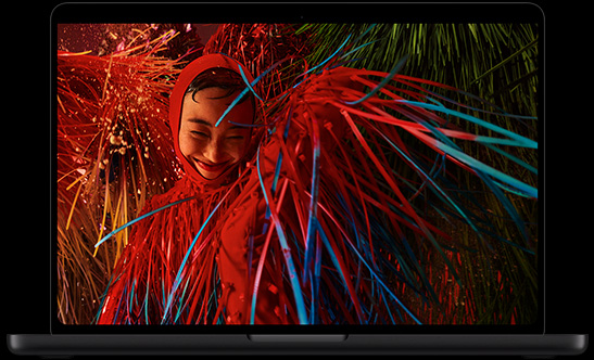 MacBook Pro mit PROLED XDR Display, Farbe Space Schwarz, geöffnet, das Display zeigt das Foto einer lächelnden Person in einem surrealen roten Outfit mit federähnlichen Details